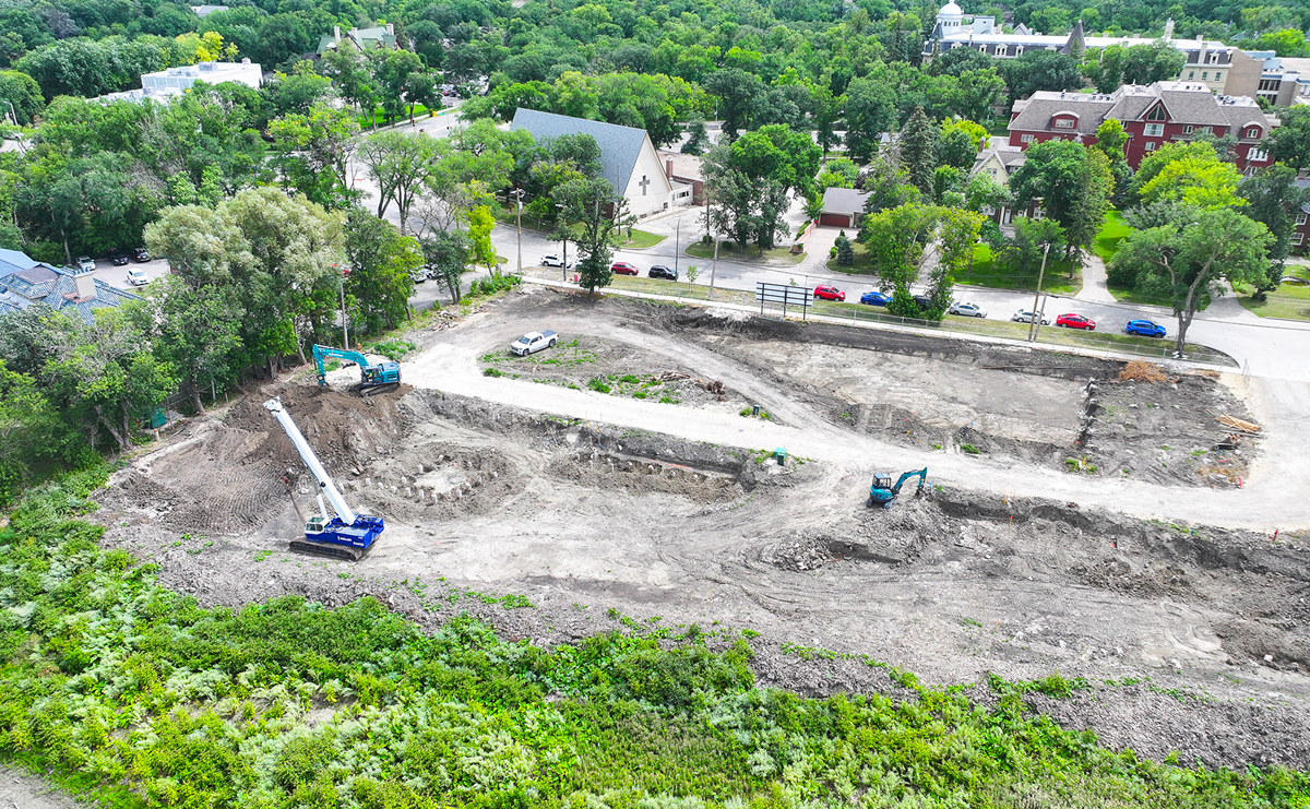 Overhead view of foundation excavation at the site with a crane and two excavators at work