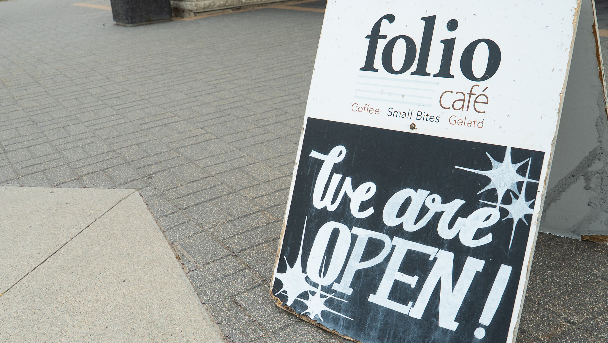 Folio Cafe sandwich board sign reading we are open on a brick sidewalk