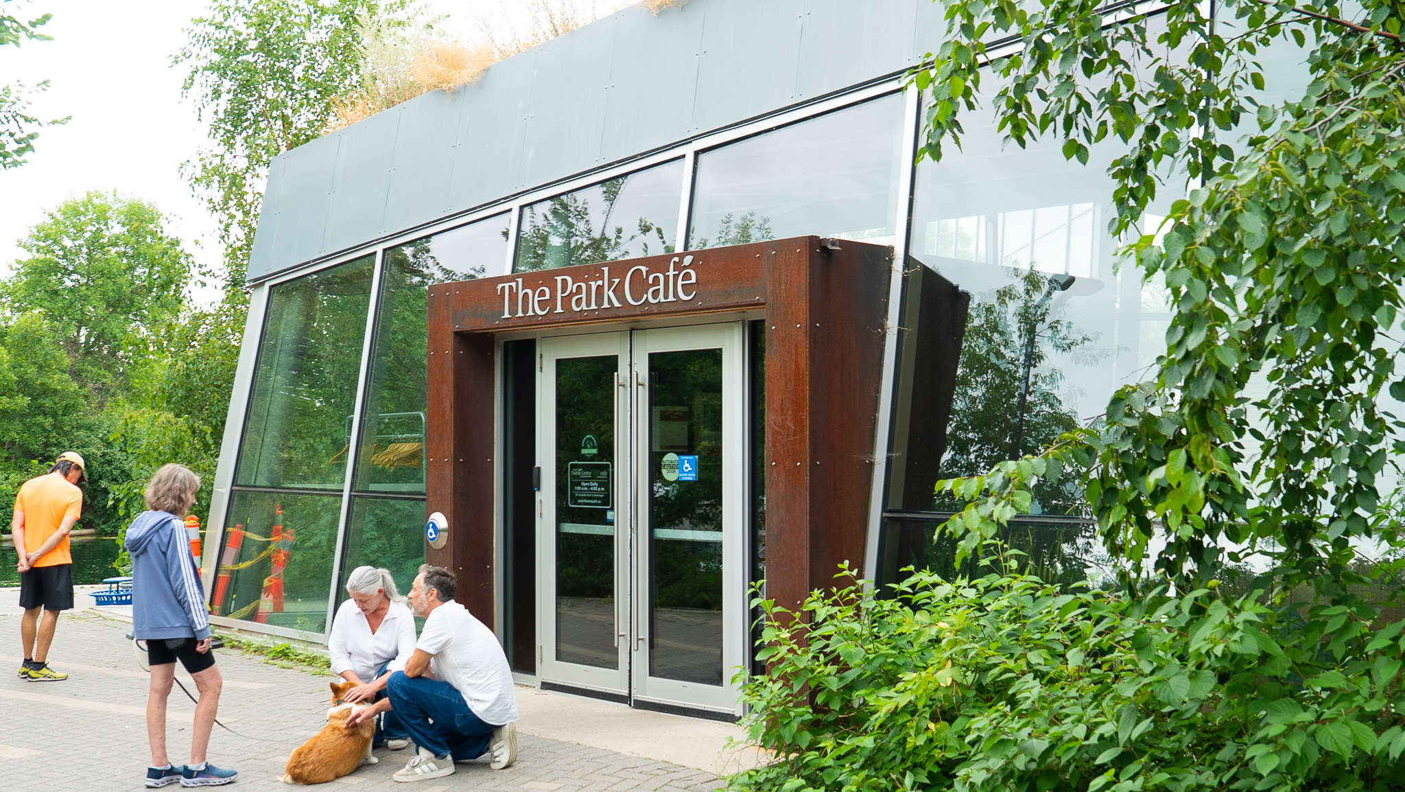 The Park Cafe entrance with weathered steel and glass, people and a dog outside